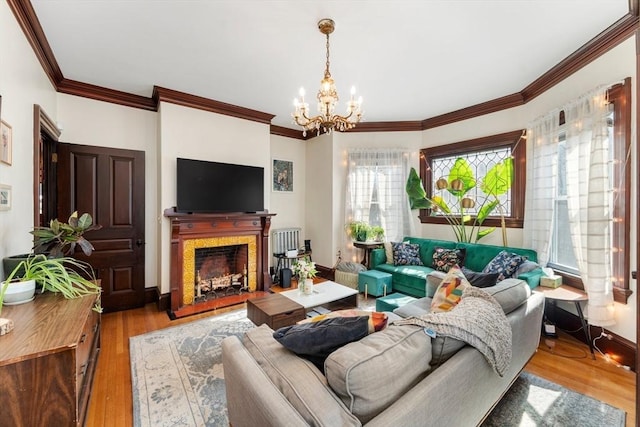 living room featuring a notable chandelier, a fireplace, baseboards, ornamental molding, and light wood-type flooring