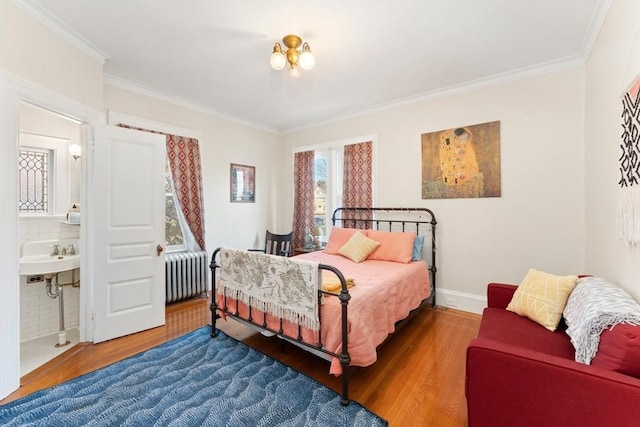 bedroom with wood finished floors, baseboards, radiator heating unit, ensuite bath, and crown molding