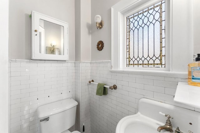 half bath featuring toilet, a sink, a wealth of natural light, and tile walls