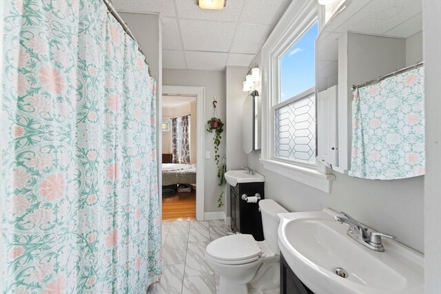 ensuite bathroom with ensuite bathroom, a drop ceiling, toilet, vanity, and marble finish floor