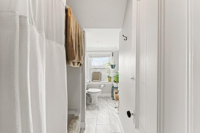 bathroom featuring toilet, marble finish floor, and a shower with curtain