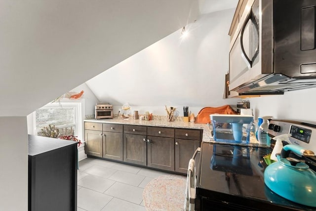 kitchen with light tile patterned floors, lofted ceiling, appliances with stainless steel finishes, light stone counters, and dark brown cabinets