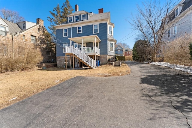 view of front of property featuring a chimney, a residential view, aphalt driveway, stairs, and a porch