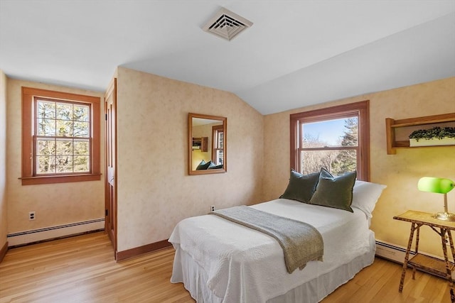 bedroom featuring visible vents, a baseboard heating unit, light wood-style floors, and vaulted ceiling