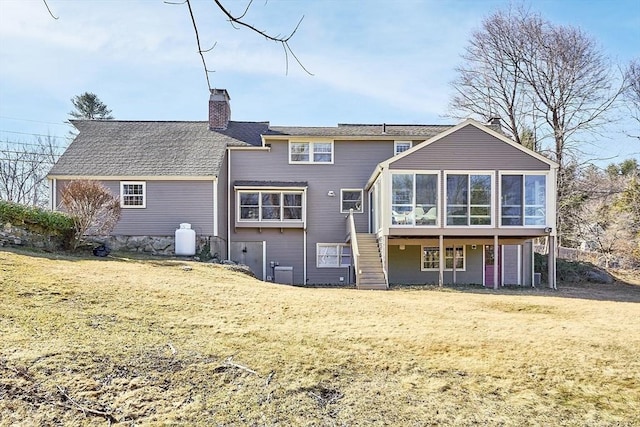 rear view of house with stairway, a lawn, a chimney, and a sunroom