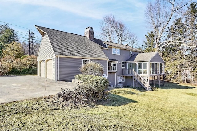 rear view of property featuring a yard, a sunroom, a chimney, concrete driveway, and a garage