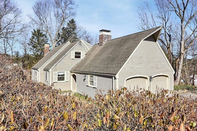 view of home's exterior with an attached garage, roof with shingles, and a chimney