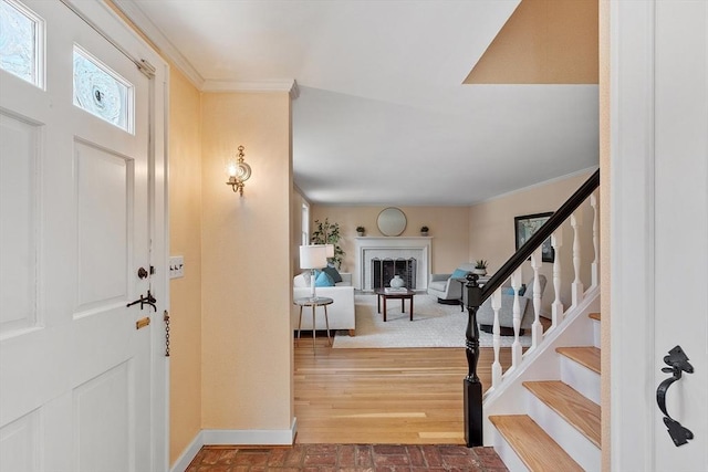 entryway with stairway, a fireplace, crown molding, brick floor, and baseboards