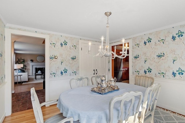 dining room with a wainscoted wall, a notable chandelier, crown molding, and wallpapered walls