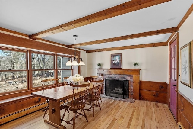 dining room featuring a wainscoted wall, beamed ceiling, a baseboard heating unit, light wood-style floors, and baseboard heating