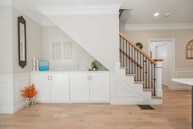 bar featuring crown molding, light hardwood / wood-style flooring, and white cabinets