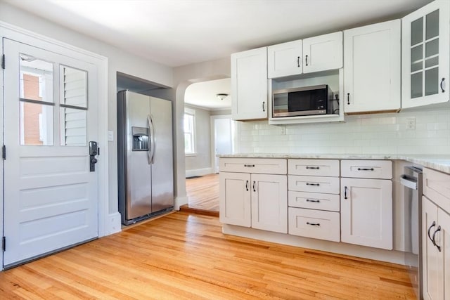 243 Bridge St, Northampton, MA 01060 - kitchen featuring appliances with stainless steel finishes, light wood finished floors, arched walkways, white cabinetry, and glass insert cabinets