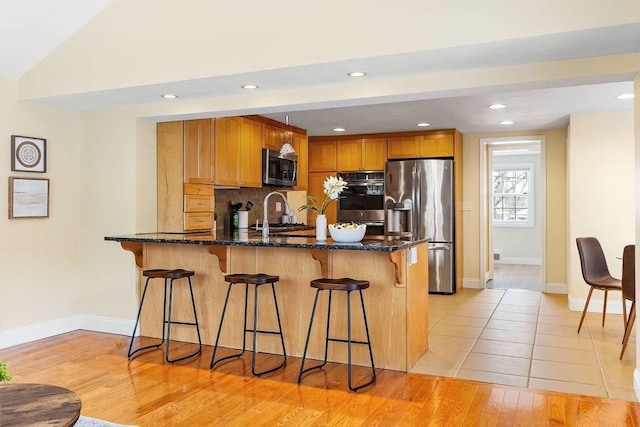 kitchen with sink, dark stone countertops, stainless steel appliances, light hardwood / wood-style floors, and a kitchen bar