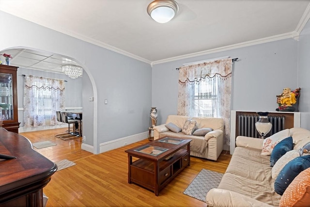 living room with arched walkways, radiator, ornamental molding, light wood-style flooring, and baseboards