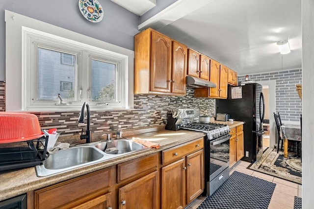 kitchen featuring gas stove, under cabinet range hood, a sink, tasteful backsplash, and light tile patterned floors