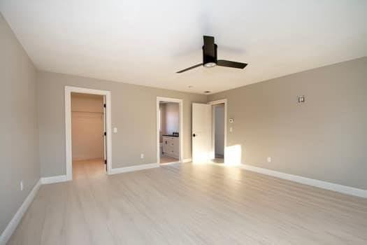 unfurnished bedroom featuring a closet, a spacious closet, ceiling fan, and light hardwood / wood-style flooring