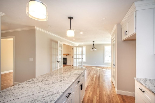 kitchen featuring hanging light fixtures, crown molding, light stone countertops, light wood-type flooring, and white cabinetry