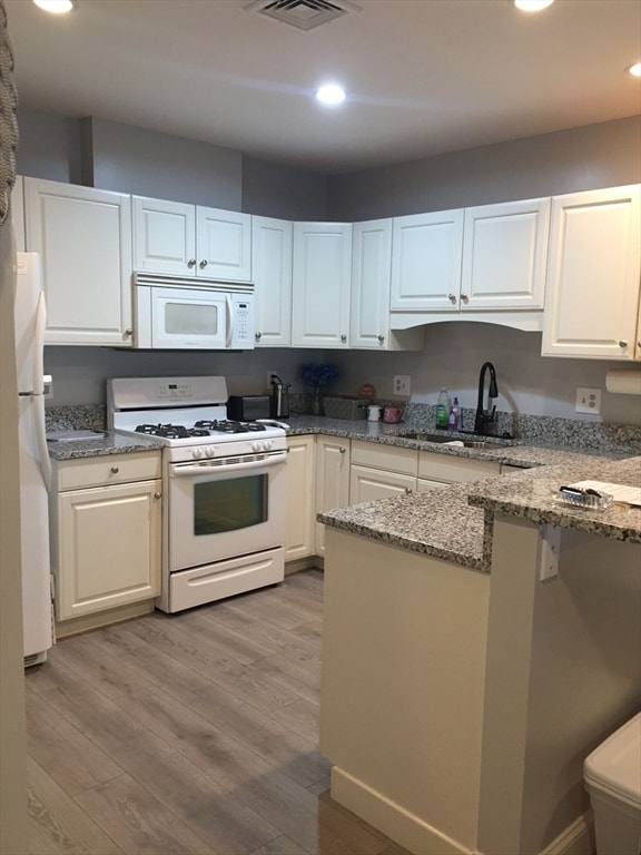 kitchen with light wood-type flooring, white appliances, light stone countertops, and white cabinets