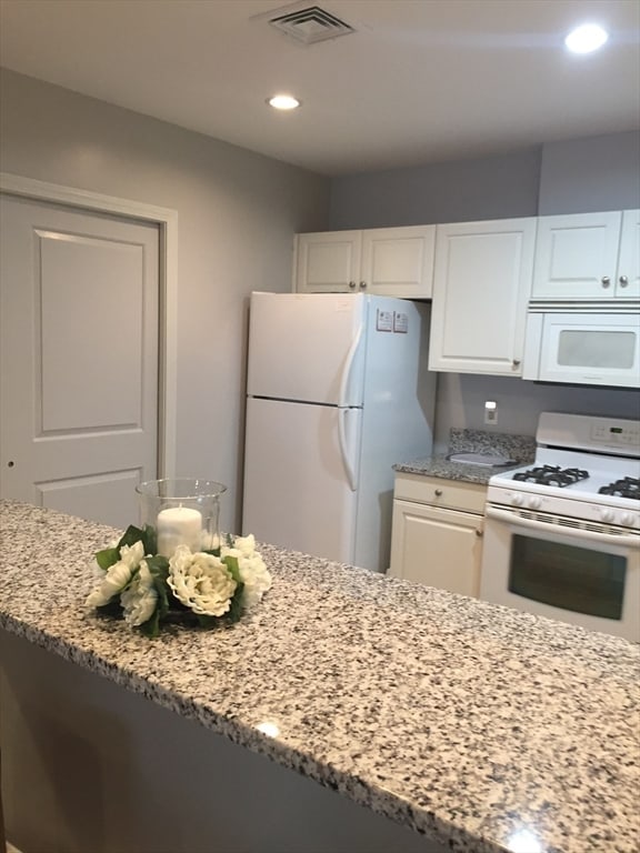 kitchen with light stone counters, white appliances, and white cabinets