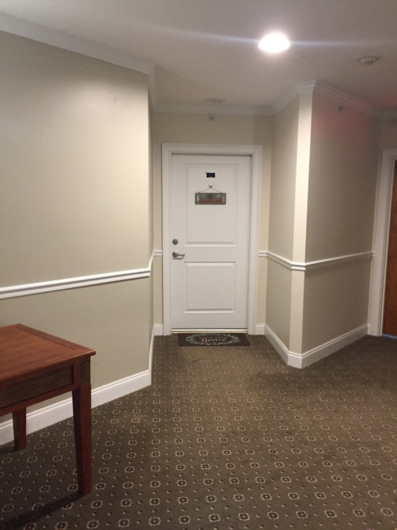 hallway featuring dark colored carpet and crown molding