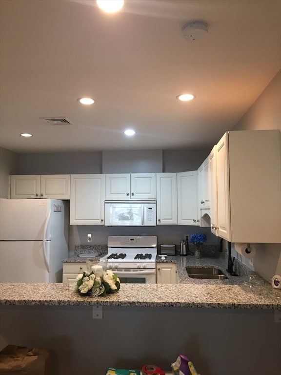 kitchen featuring dark stone counters, sink, white appliances, and white cabinetry