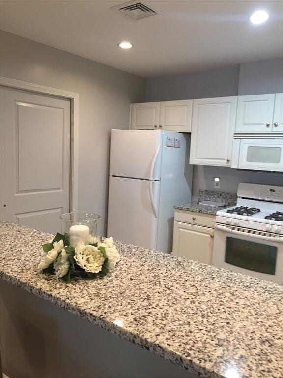 kitchen with white appliances, visible vents, white cabinets, and light stone counters