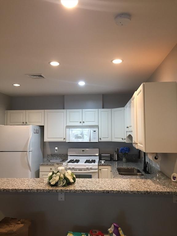 kitchen featuring stone counters, white appliances, a sink, visible vents, and white cabinetry