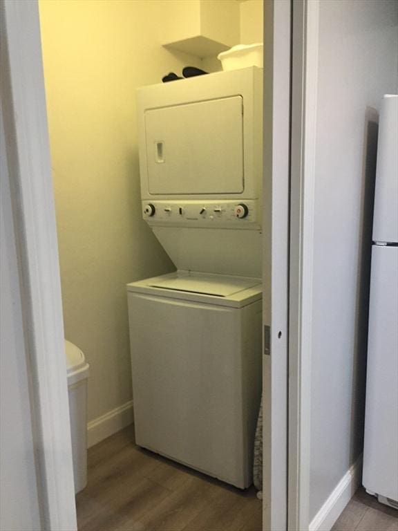 clothes washing area with light wood-type flooring, laundry area, baseboards, and stacked washer / dryer