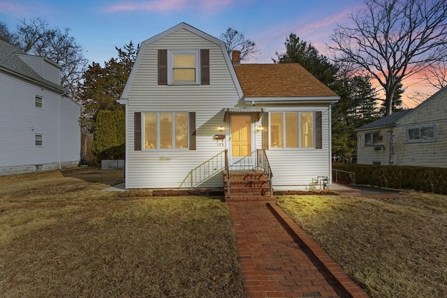 colonial inspired home featuring a yard, a gambrel roof, a chimney, and a shingled roof