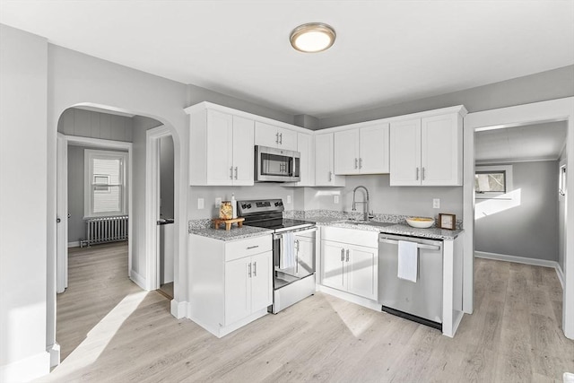 kitchen featuring white cabinets, radiator heating unit, light wood-style flooring, and appliances with stainless steel finishes