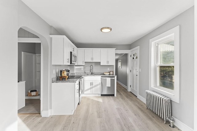 kitchen featuring light wood finished floors, radiator heating unit, a sink, stainless steel appliances, and white cabinets