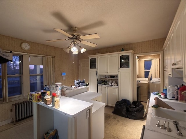 kitchen featuring sink, white cabinets, ceiling fan, radiator, and washer and clothes dryer