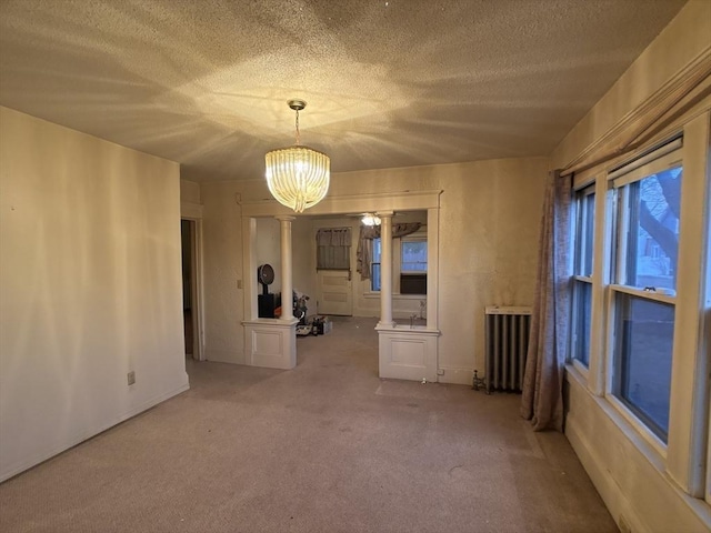 empty room with a notable chandelier, radiator heating unit, carpet floors, and a textured ceiling