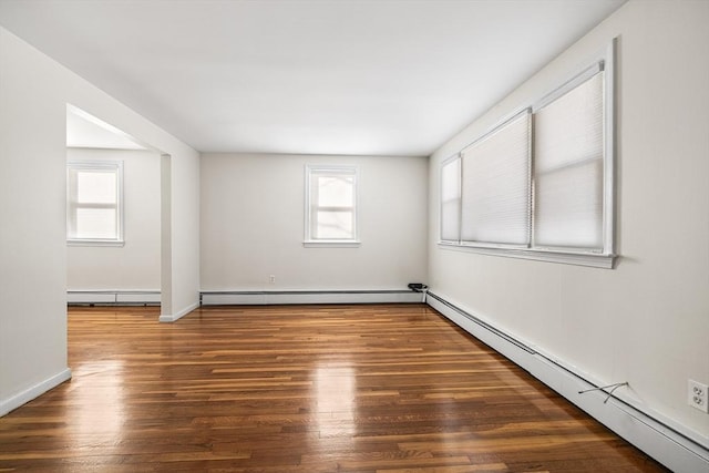 empty room featuring baseboard heating, plenty of natural light, and dark wood-type flooring