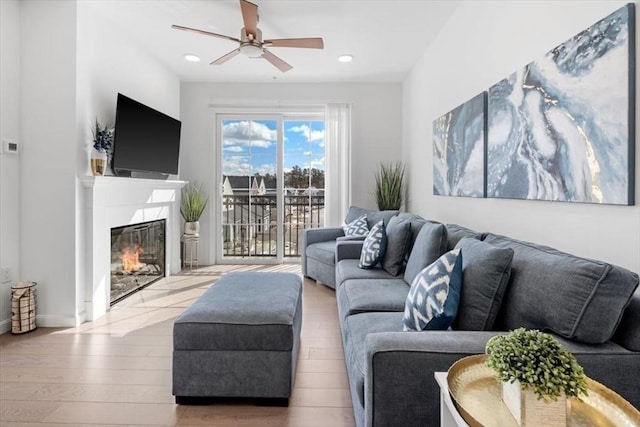 living room featuring light wood-type flooring, a premium fireplace, and ceiling fan