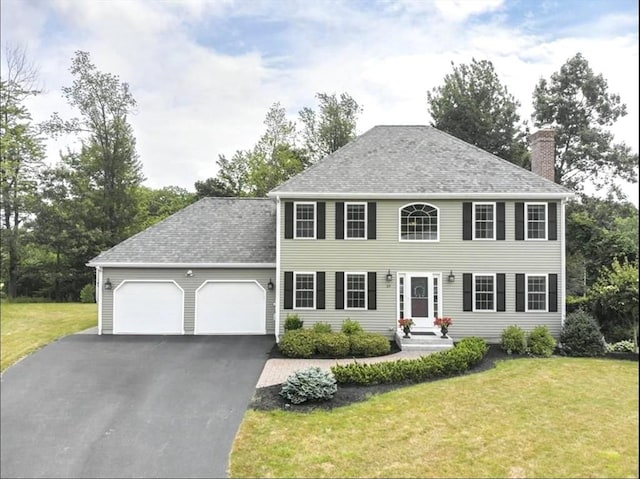 colonial inspired home featuring driveway, a chimney, a front lawn, and a garage