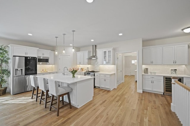 kitchen with appliances with stainless steel finishes, pendant lighting, white cabinets, a kitchen island with sink, and wall chimney exhaust hood