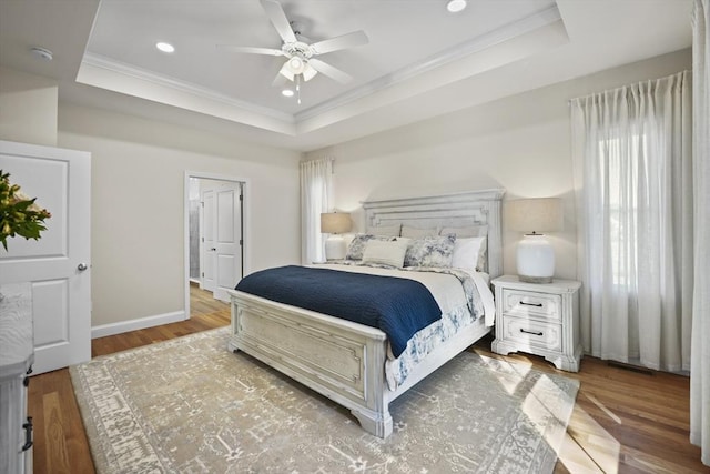 bedroom featuring a raised ceiling, ornamental molding, hardwood / wood-style floors, and ceiling fan