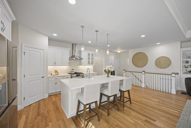 kitchen with a center island with sink, white cabinetry, pendant lighting, and wall chimney exhaust hood