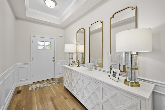 entryway with crown molding, a raised ceiling, and light wood-type flooring