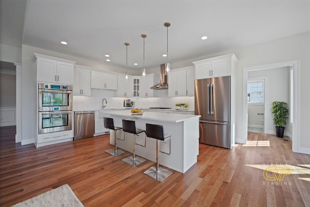 kitchen with a kitchen island, appliances with stainless steel finishes, pendant lighting, white cabinets, and wall chimney range hood