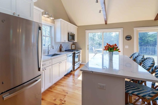 kitchen featuring a breakfast bar, sink, vaulted ceiling, stainless steel appliances, and white cabinets