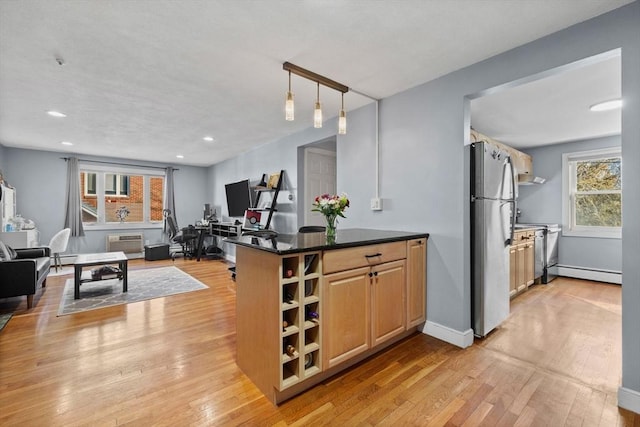 kitchen with light brown cabinetry, light hardwood / wood-style floors, a baseboard heating unit, decorative light fixtures, and stainless steel fridge