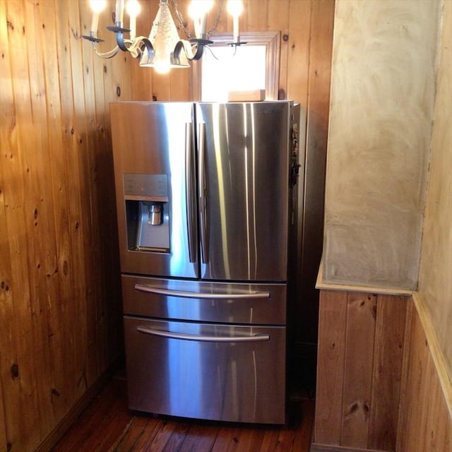 interior details featuring dark wood-type flooring, a notable chandelier, wooden walls, and stainless steel fridge with ice dispenser