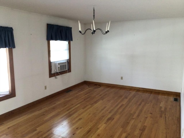 unfurnished room with a healthy amount of sunlight, dark wood-type flooring, an inviting chandelier, and cooling unit