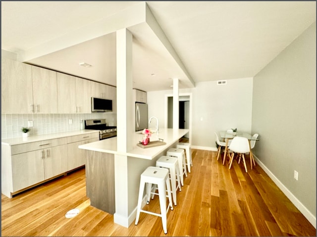 kitchen with a kitchen bar, light wood-type flooring, tasteful backsplash, stainless steel appliances, and a center island with sink