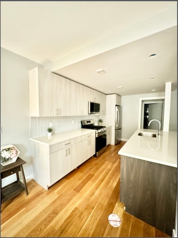 kitchen with decorative backsplash, light wood-type flooring, sink, and appliances with stainless steel finishes