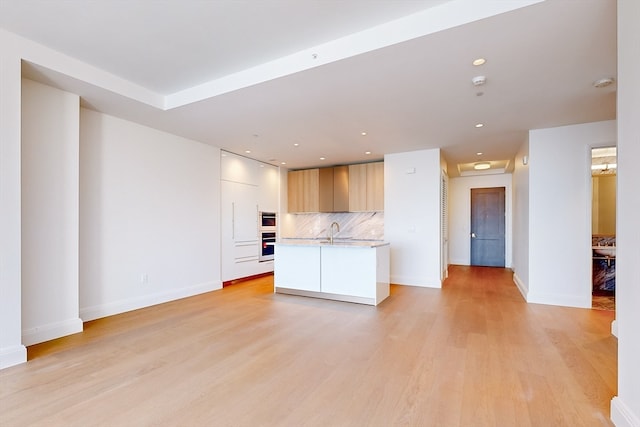 kitchen featuring oven, light hardwood / wood-style flooring, sink, an island with sink, and tasteful backsplash