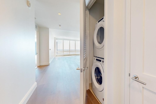 laundry room with stacked washer and dryer, light wood-style flooring, laundry area, and baseboards