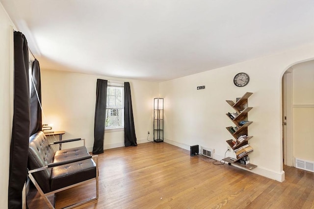 living area with arched walkways, light wood-style floors, and baseboards